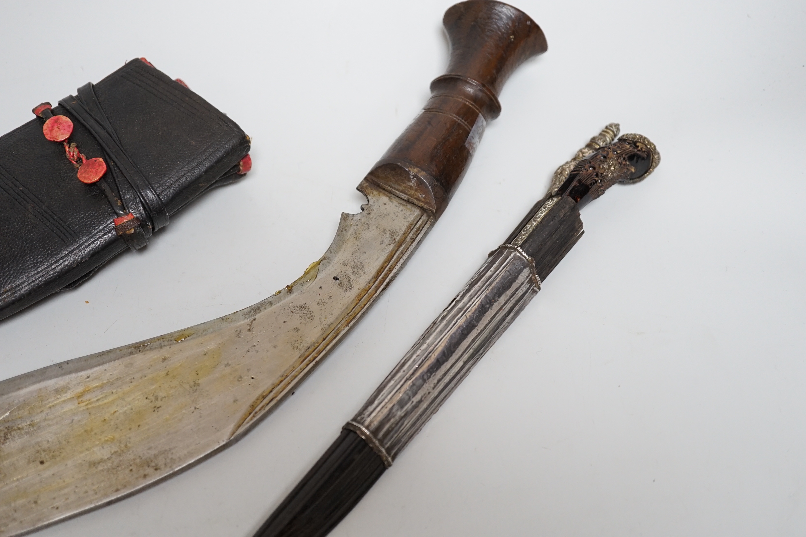 Two Sinhalese daggers and a kukri, a silver inlaid Kirichchiya dagger, together with another in a scabbard with a long pin, another dagger with a wooden handle, a head of a brass inlaid iron pole arm, a George V 1897 pat